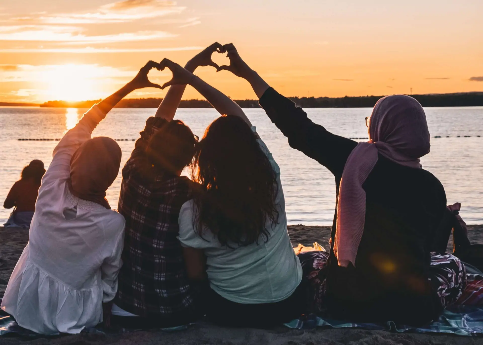 A photo of group of friends enjoying the sunset at the bay doing love sign with their hands.