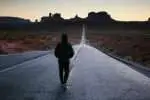 A person in the center of an open highway walking.
