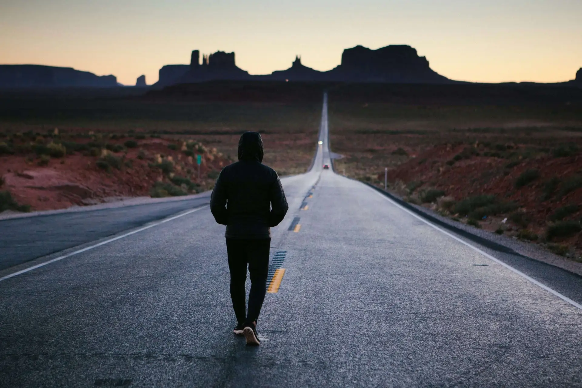 A person in the center of an open highway walking.