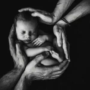 This captivating black and white photograph portrays an intimate moment of hands gently holding a baby. The composition emphasizes the tender connection between the child and the caregiver, encapsulating a timeless moment of care and protection.