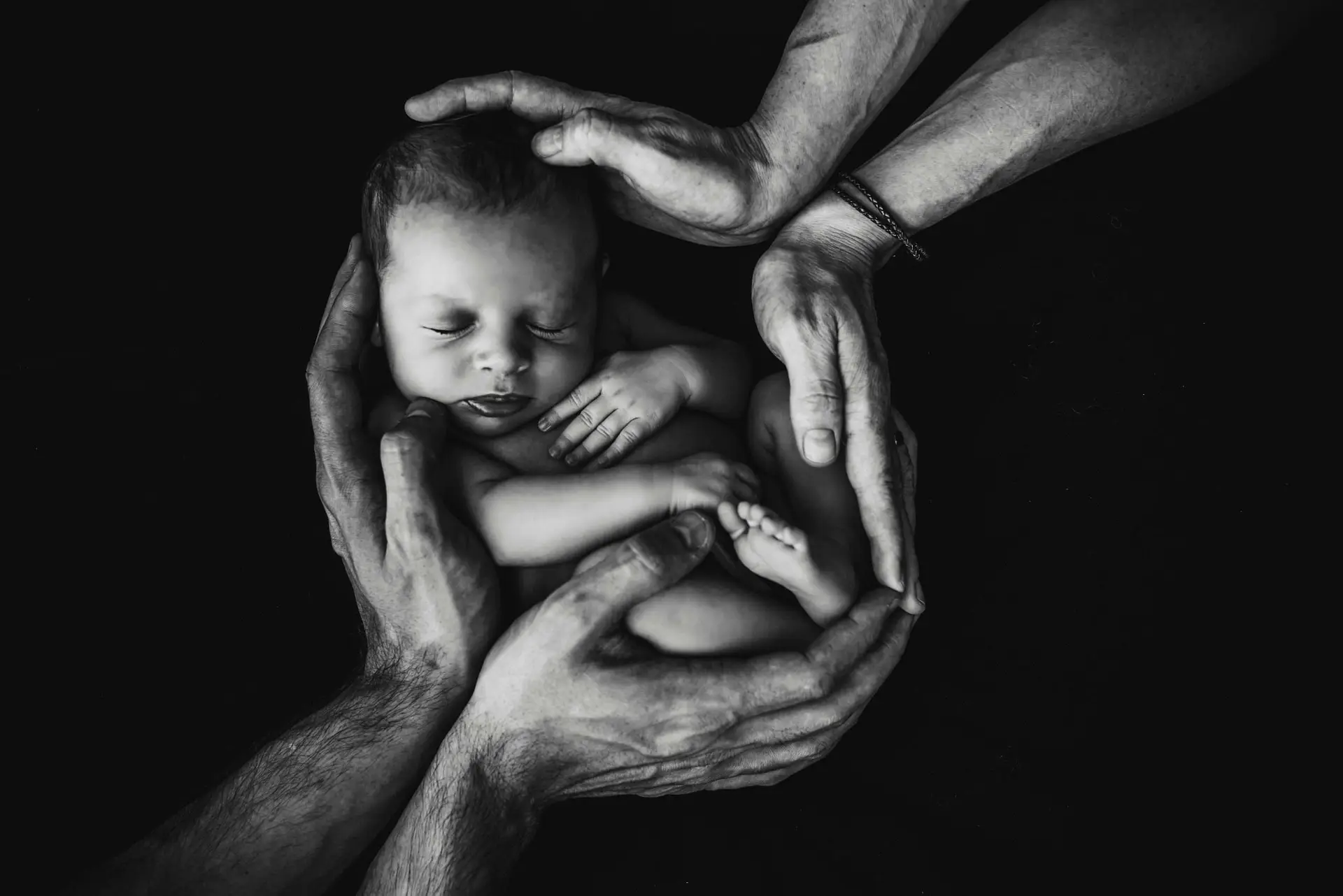 This captivating black and white photograph portrays an intimate moment of hands gently holding a baby. The composition emphasizes the tender connection between the child and the caregiver, encapsulating a timeless moment of care and protection.