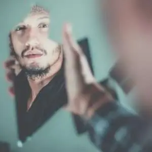 Man looking in a broken piece of a glass while holding it.