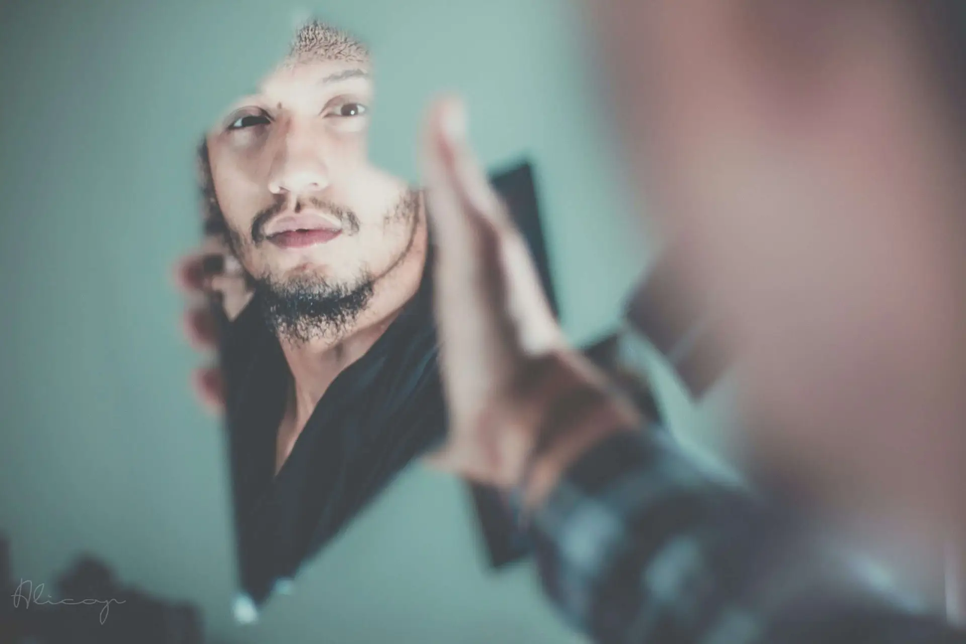 Man looking in a broken piece of a glass while holding it.