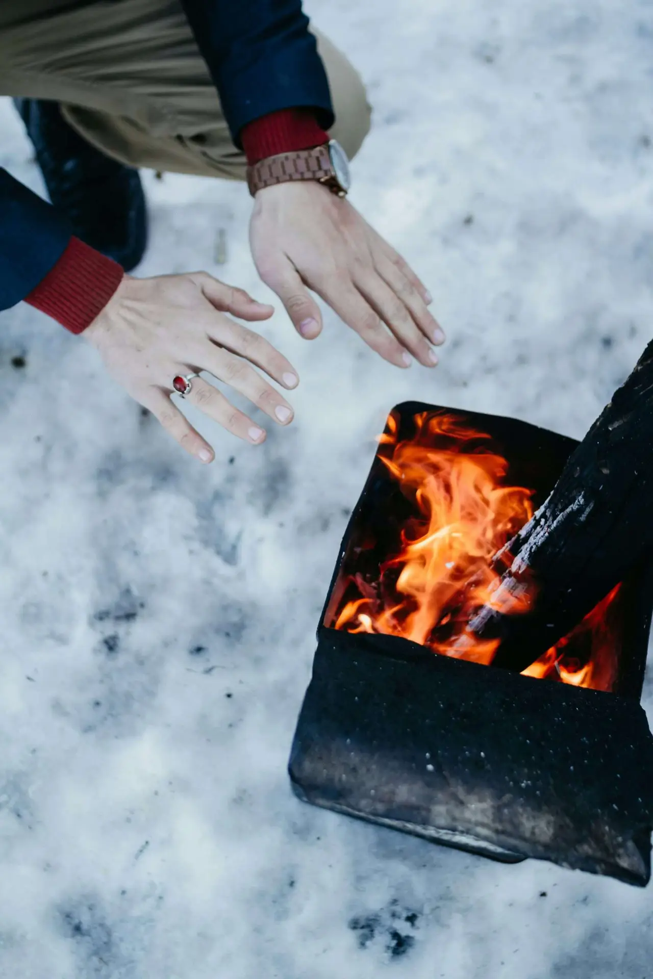 A hand close to a fire pit warming it in a snowy season.