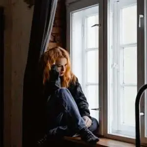 A woman sitting in the windowpane thinking hard about something.