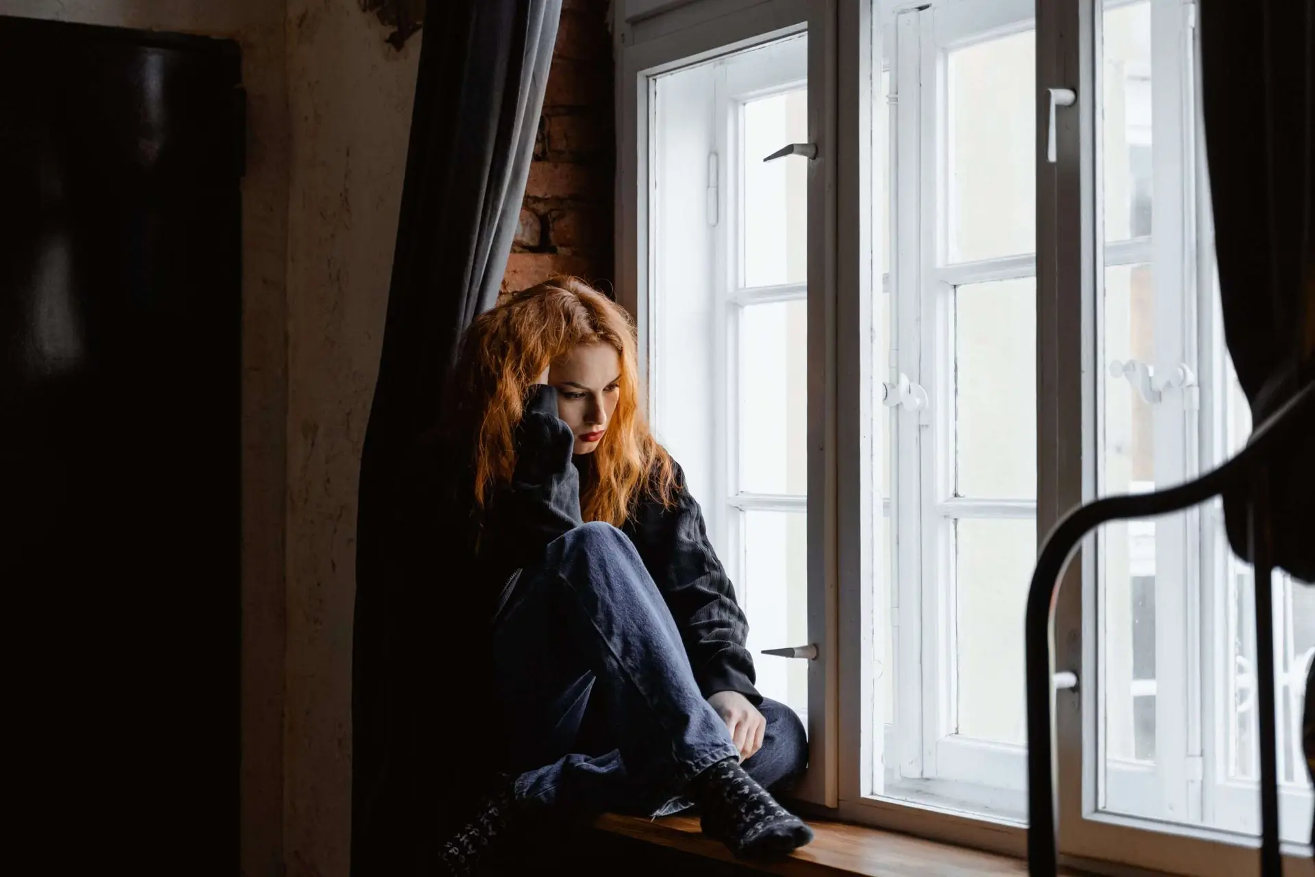A woman sitting in the windowpane thinking hard about something.